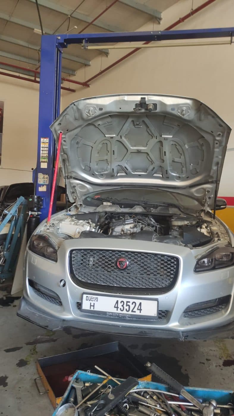 A car raised on a two-post lift with the bonnet open for engine bay work